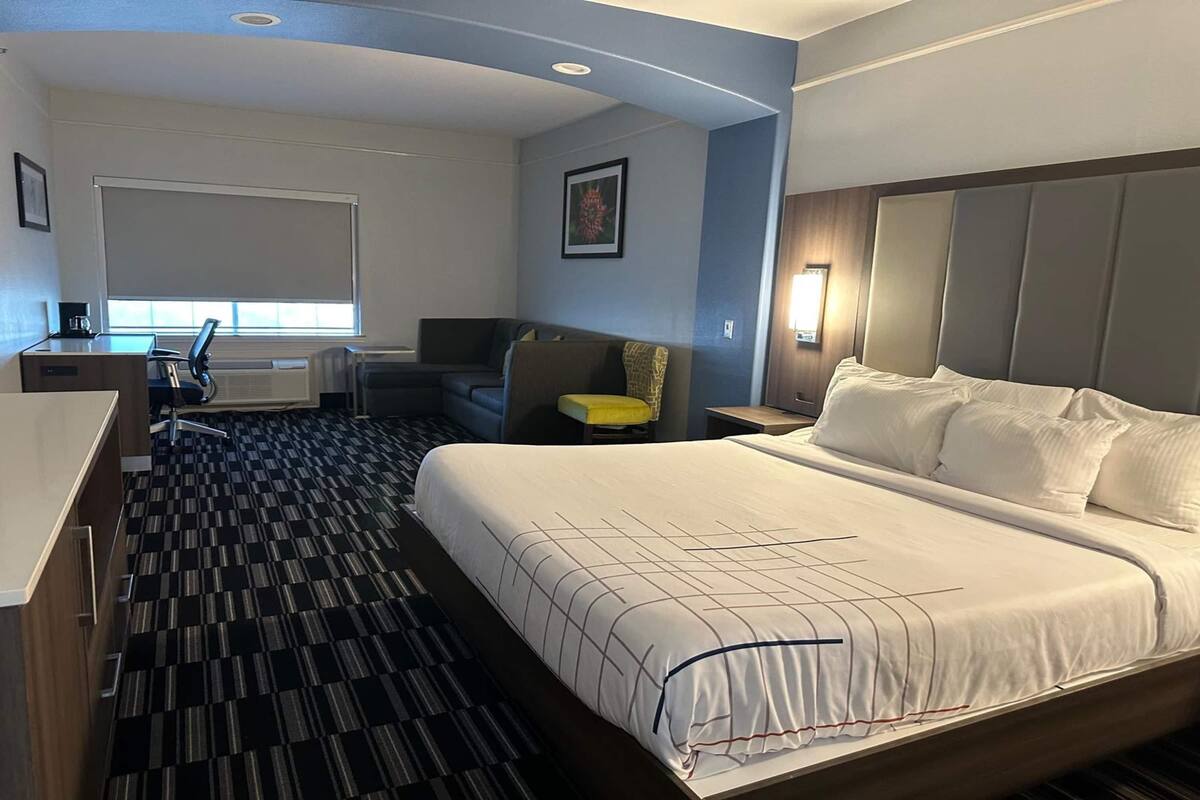 A hotel room with a large bed, a desk, a chair, and a sofa.