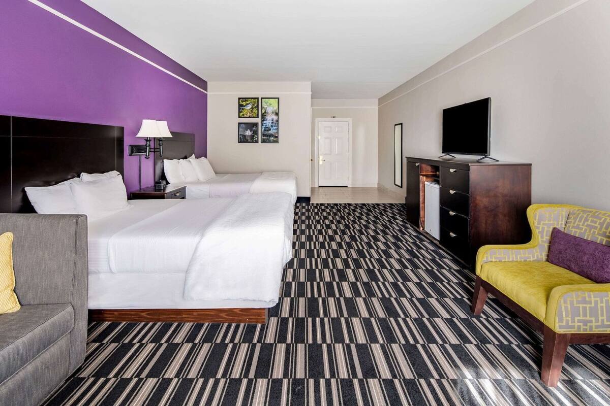 A hotel room with two beds, a sofa, a TV, and a desk.