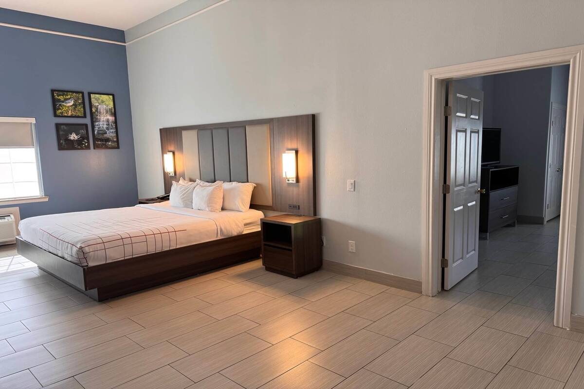 A bedroom with a bed, bedside tables, and a TV in the adjacent room.