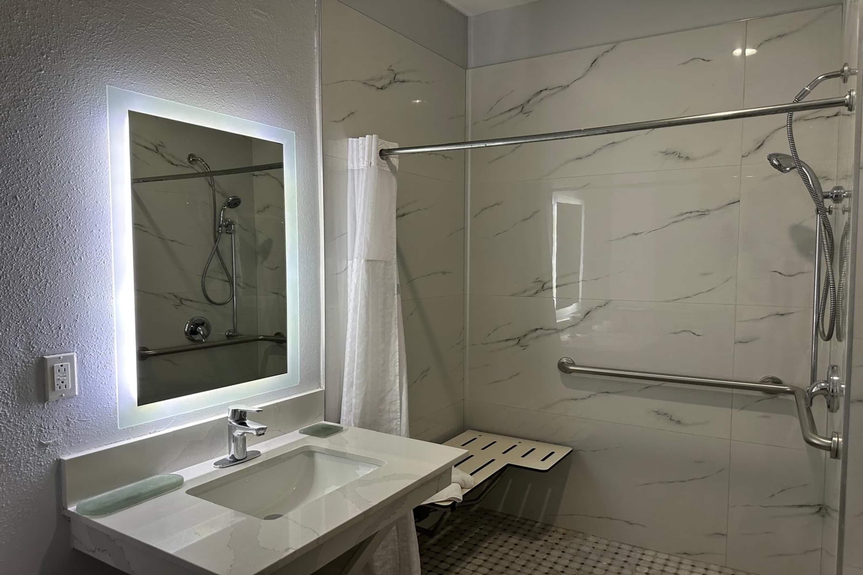 Un baño moderno con ducha envuelta en vidrio, tocador con espejo y paredes con diseño de mármol.