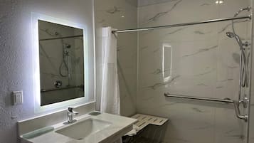 A modern bathroom with a glass-enclosed shower, a vanity with a mirror, and marble-patterned walls.