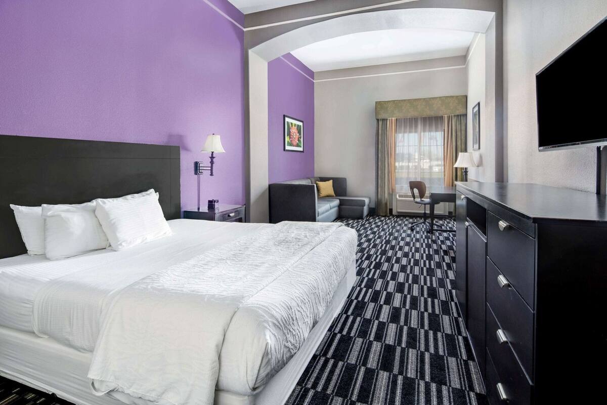 A hotel room with a large bed, a desk, a chair, a TV, and a wardrobe.