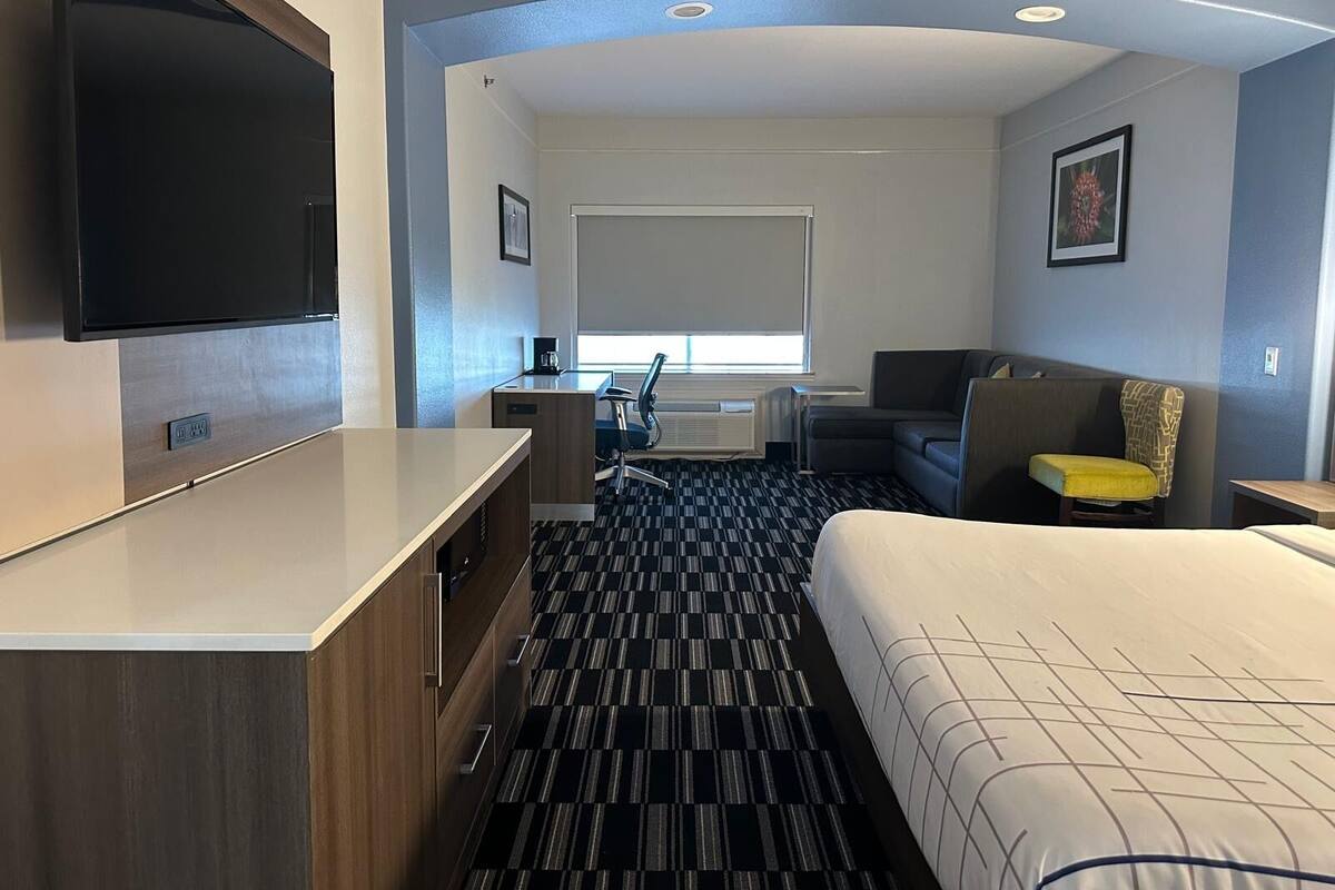 A hotel room with a bed, a desk, a chair, a television, and a window with blinds.