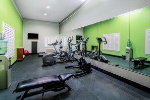 Un gimnasio con equipo de ejercicio, una banca, un dispensador de agua y un televisor en la pared.