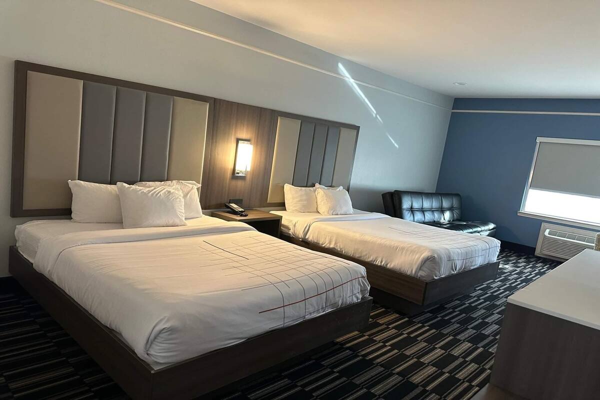 A hotel room with two beds, a desk, a chair, and a large window.