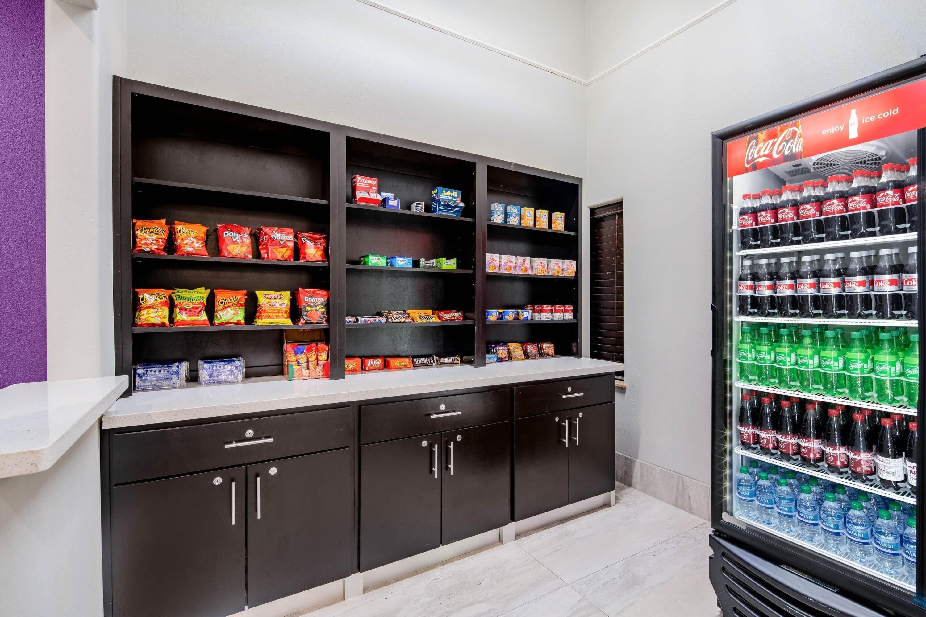 A snack and drink vending area with multiple shelves of snacks and a Coca-Cola refrigerator.
