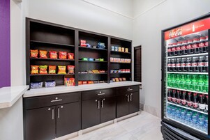 Zona de venta automática con aperitivos y bebidas, con varias estanterías llenas de productos y un refrigerador de Coca-Cola.