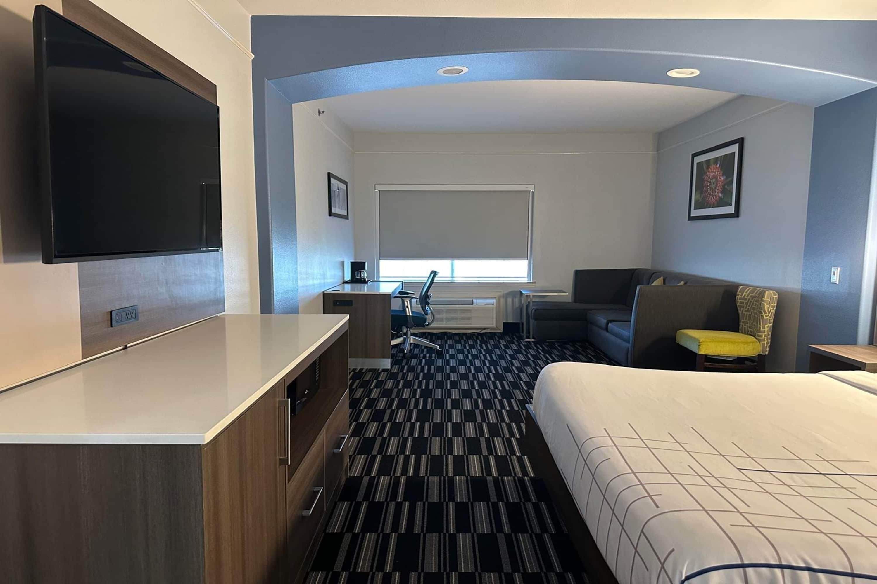 A hotel room with a bed, a desk, a chair, a TV, and a window with blinds.