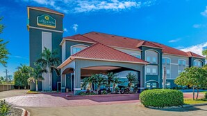 A hotel with a prominent sign, a covered entrance, and a landscaped area with palm trees. - La Quinta Inn & Suites by Wyndham Alamo - McAllen East (Alamo)