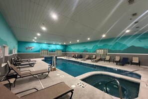 Una piscina interior con sillones de descanso, un trampolín y un mural de paisaje submarino.