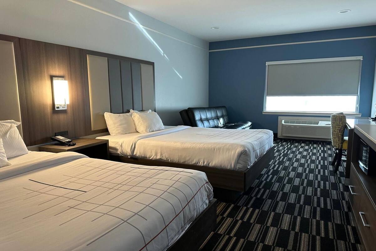 A hotel room with two beds, a desk, a chair, a TV, and a large window.