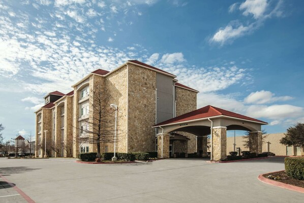 A multi-story hotel with a stone facade and red roof, featuring a covered entrance and a parking lot.