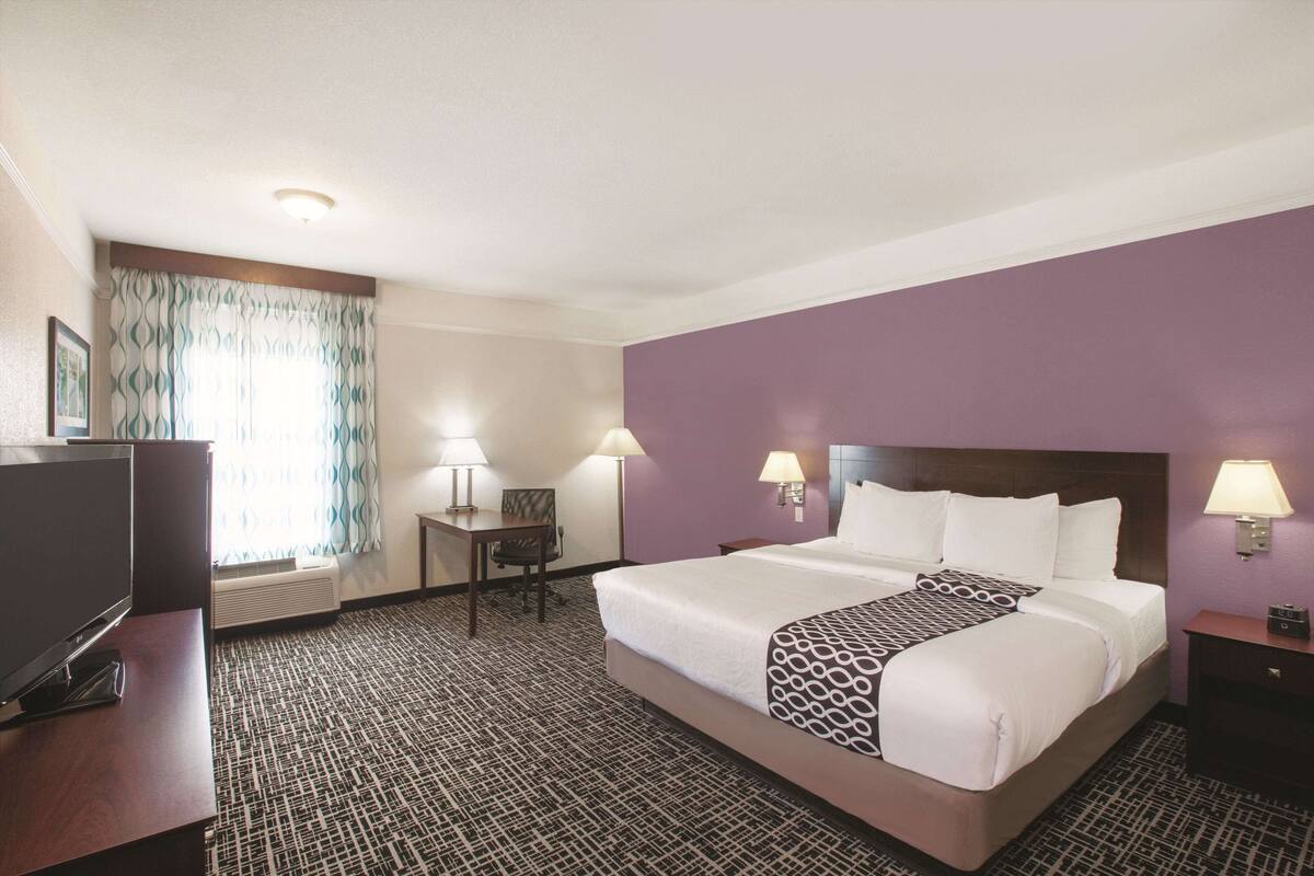 A hotel room with a large bed, a desk, and a television.