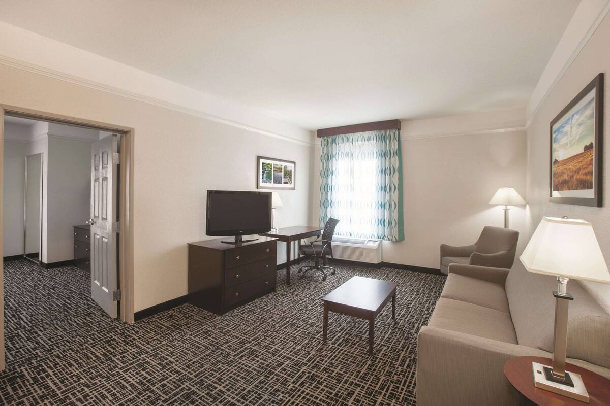 A hotel room with a desk, television, sofa, and lamps.