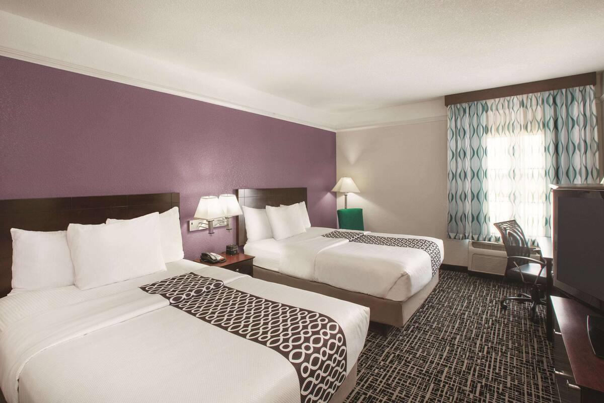 A hotel room with two beds, a desk, a chair, a TV, and a window with curtains.