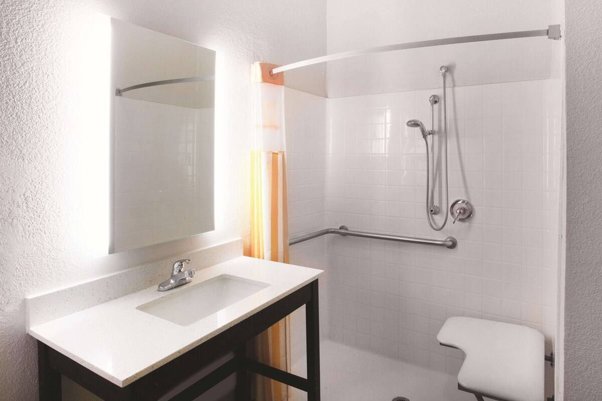 A bathroom with a white sink, a mirror, a shower with a grab bar, and a white toilet.