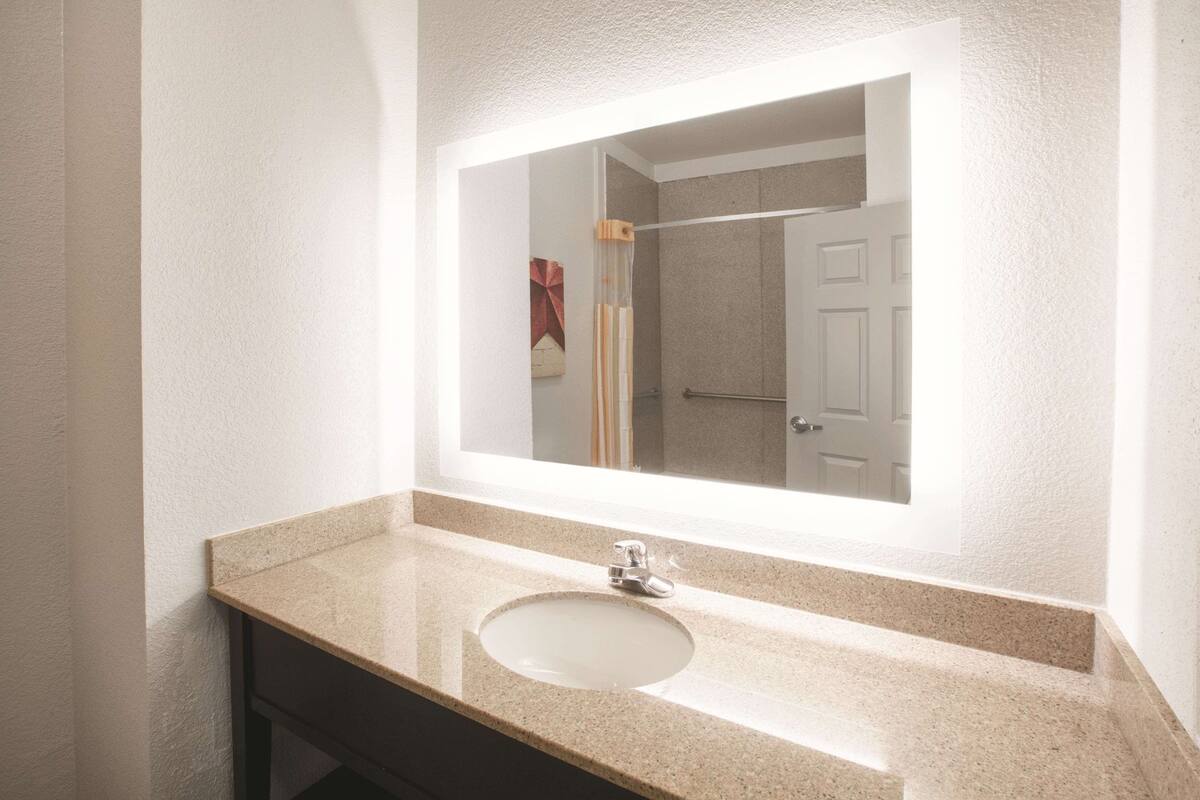 A bathroom with a large mirror, a sink, and a shower area.