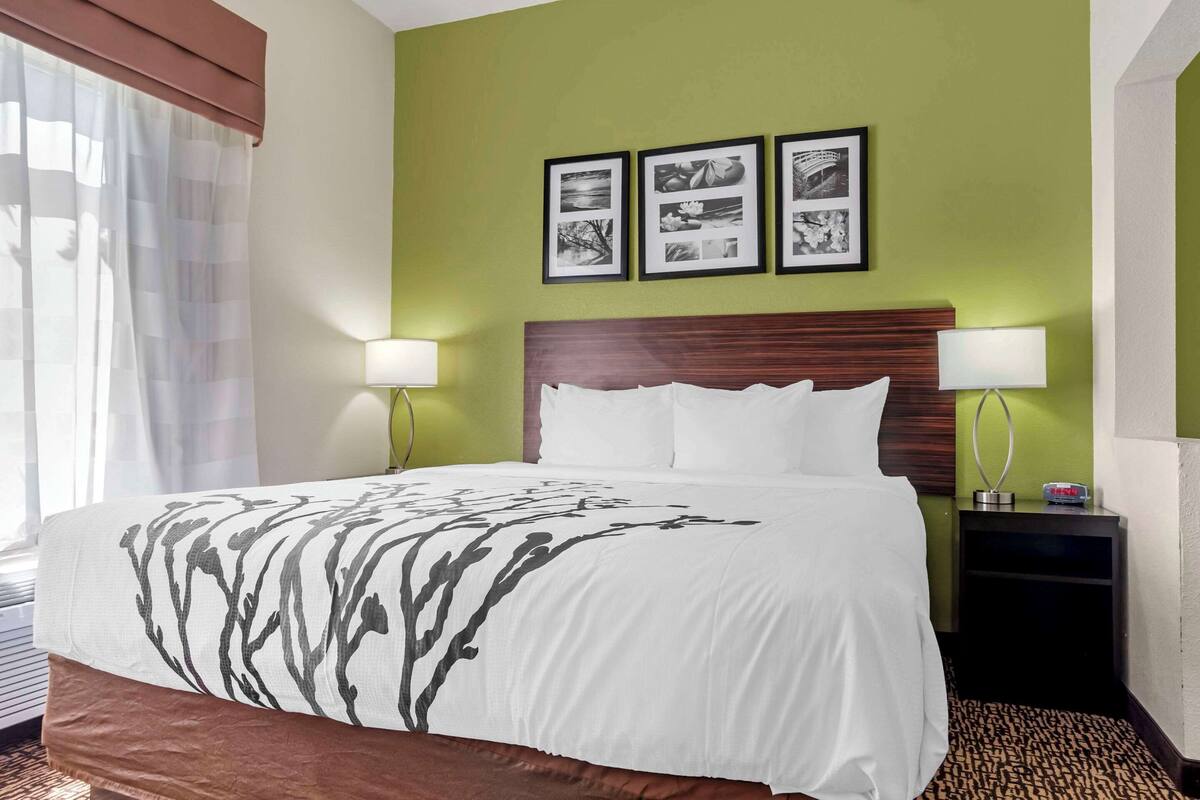 A hotel room with a large bed, two bedside lamps, a nightstand, and three framed pictures on the wall.