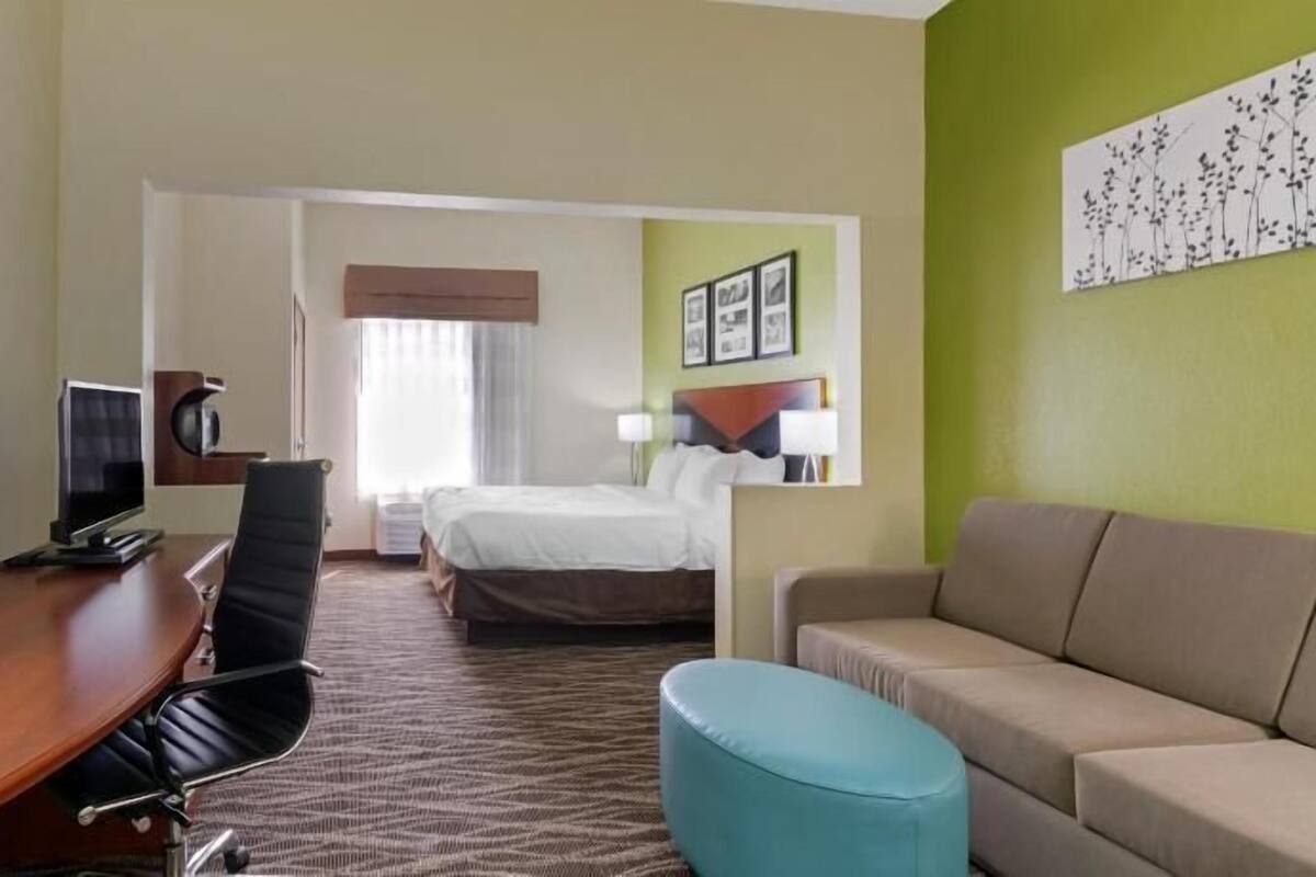 A hotel room with a desk, chair, bed, and a couch.