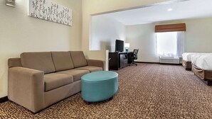 A hotel room with a sofa, ottoman, flat-screen TV, desk, and a bed. - Sleep Inn & Suites Montgomery East I-85 (Montgomery)