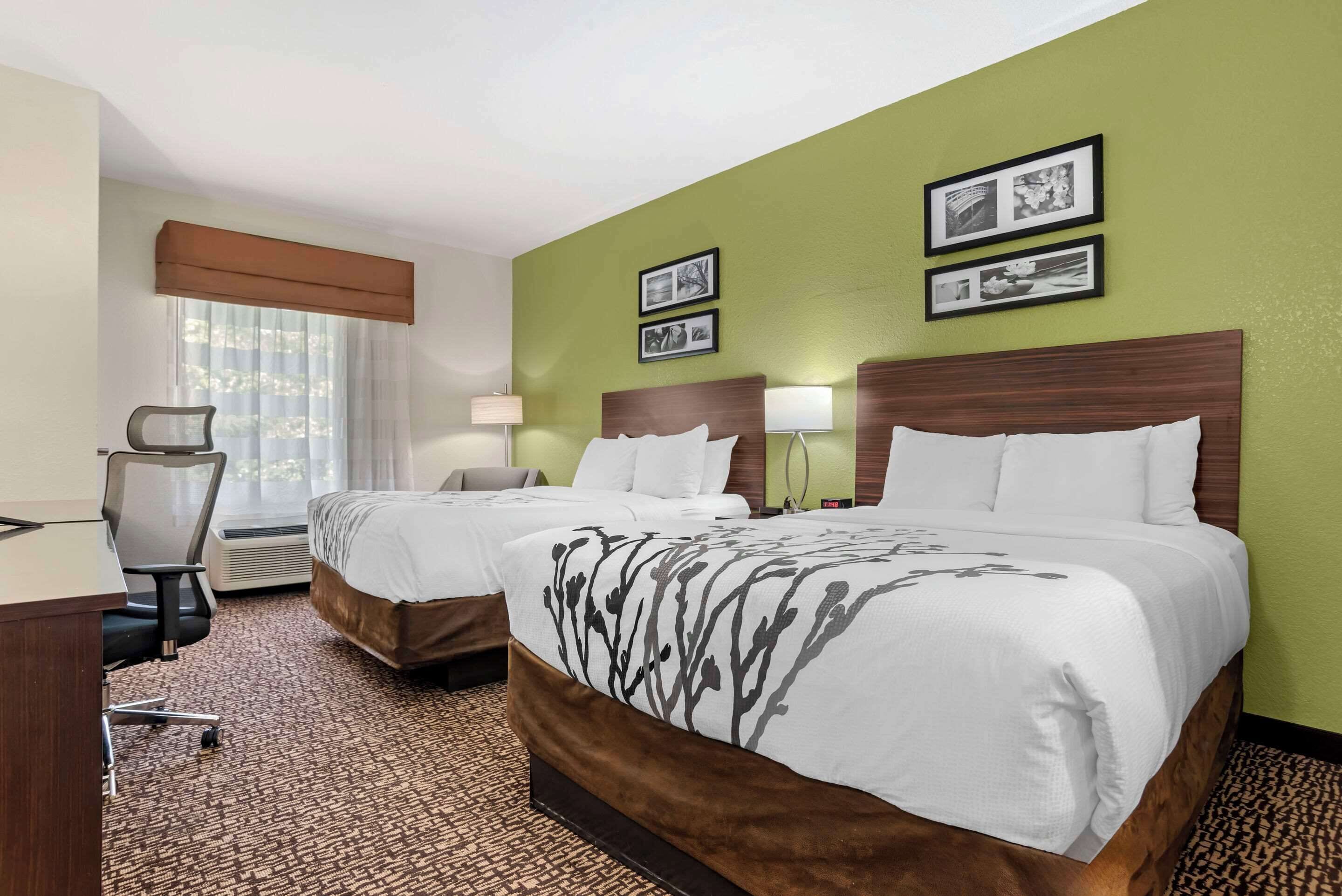 Une chambre d’hôtel avec deux lits, un bureau, une chaise et une fenêtre avec des stores.