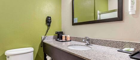 A bathroom with a white toilet, a granite countertop sink, a mirror, and a hairdryer plugged in.