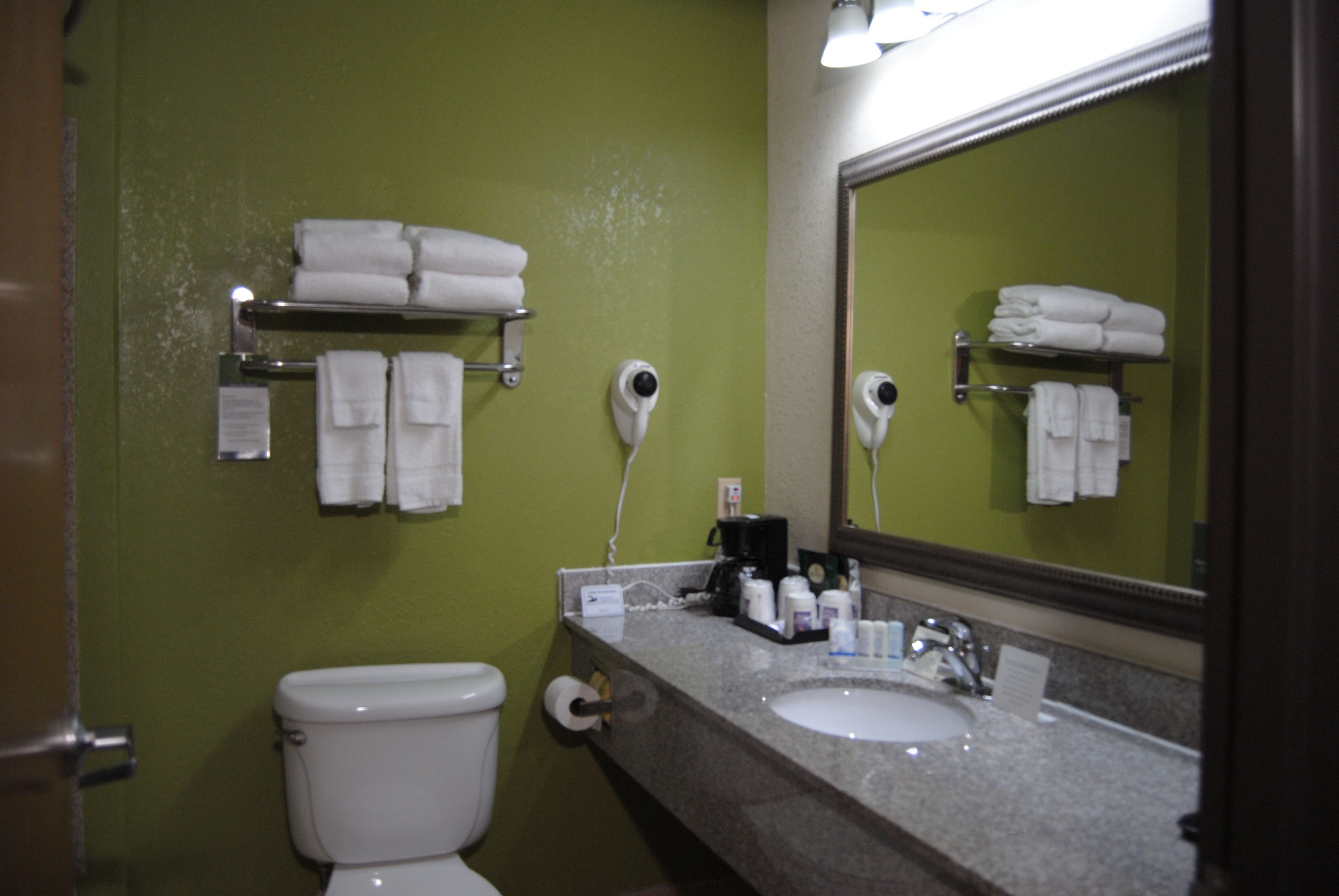 A bathroom with a green wall, a white toilet, a sink with a mirror, and towel racks with folded towels.