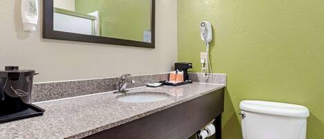 A bathroom with a granite countertop sink, a mirror, a hairdryer, and a toilet.