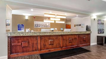 A reception area with a wooden counter, a black mat, and a wall with framed pictures and a sign.