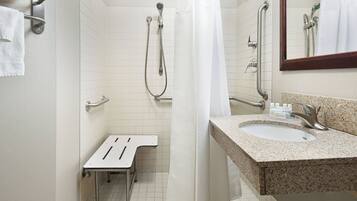 A bathroom with a shower, a sink, a mirror, and a grab bar.