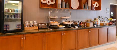 A buffet setup with various food items and beverages, a refrigerated display case, and a shelf with decorative items.