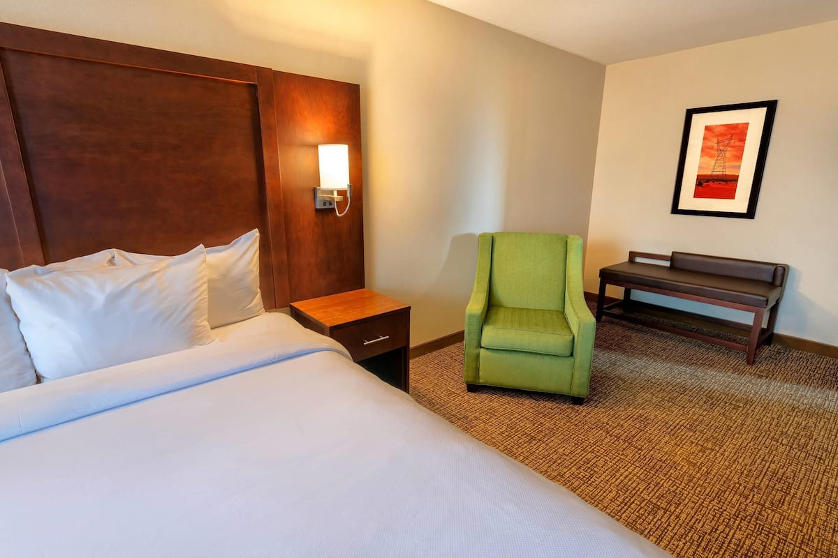 Ein Hotelzimmer mit einem großen Bett, einem grünen Sessel, einem kleinen Tisch und einem gerahmten Bild an der Wand.