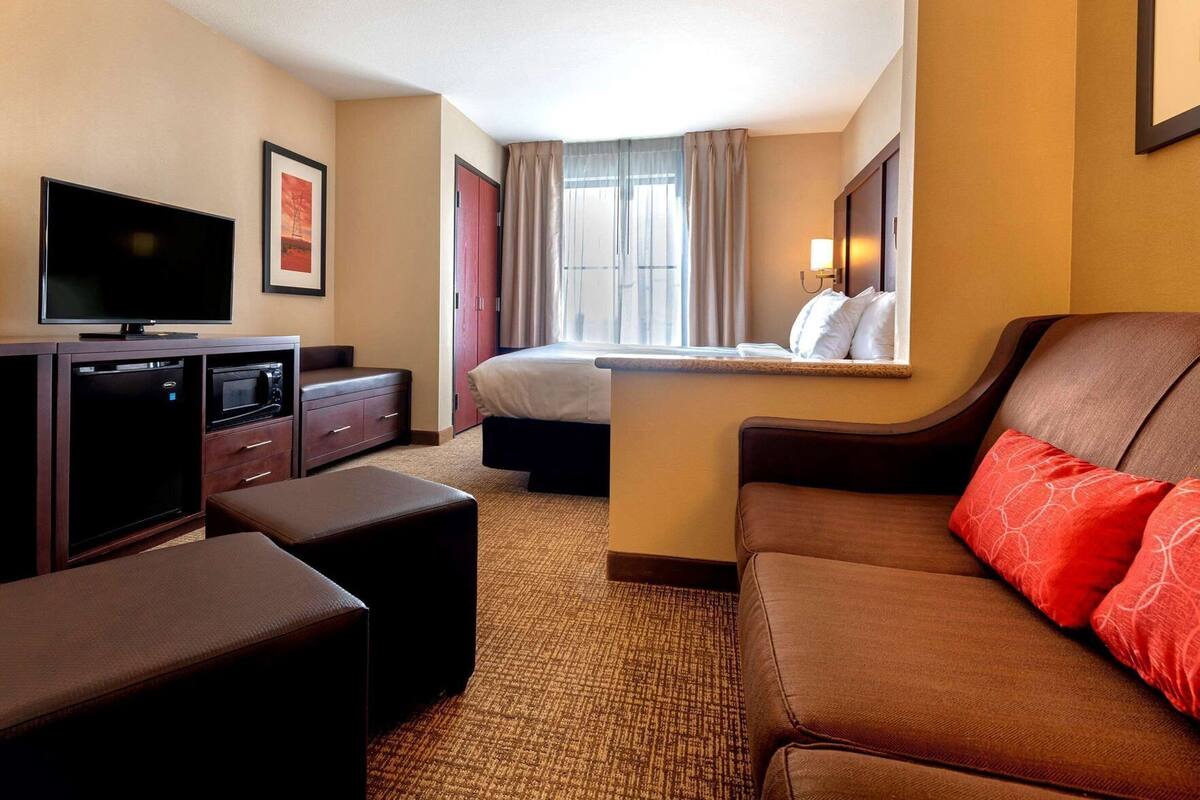Ein Hotelzimmer mit Bett, Fernseher, Schreibtisch mit Computer, Sofa und einem Fenster mit Vorhängen.