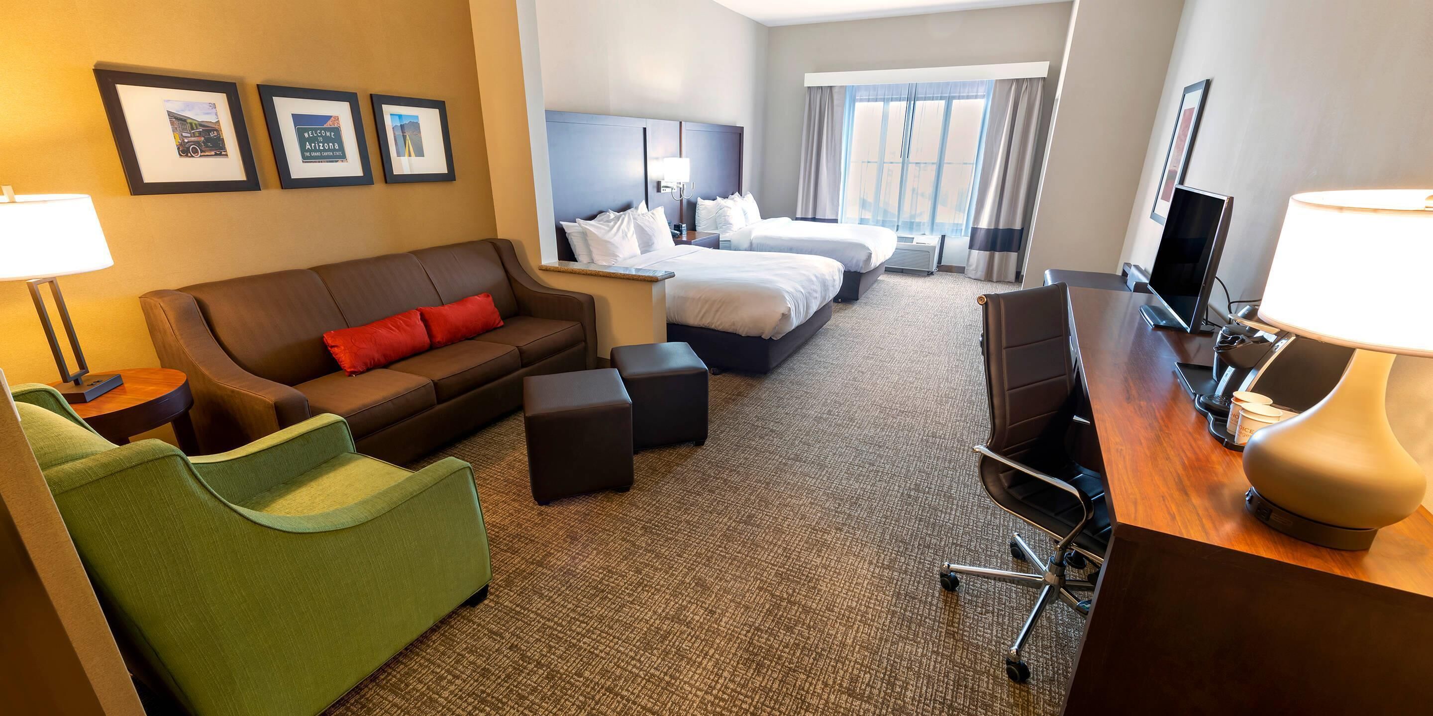 Habitación de hotel con sofá, dos camas, escritorio con lámpara, televisión y cuadros en la pared.