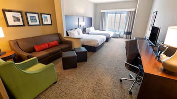 Habitación de hotel con sofá, dos camas, escritorio con lámpara, televisión y cuadros en la pared.