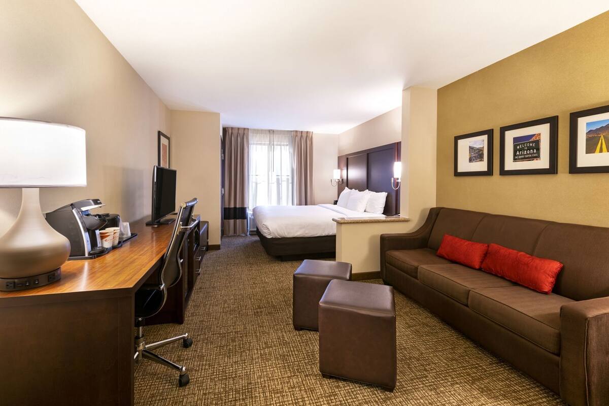 Ein Hotelzimmer mit einem Bett, einem Schreibtisch mit Lampe, einer Couch und einer Kaffeemaschine.
