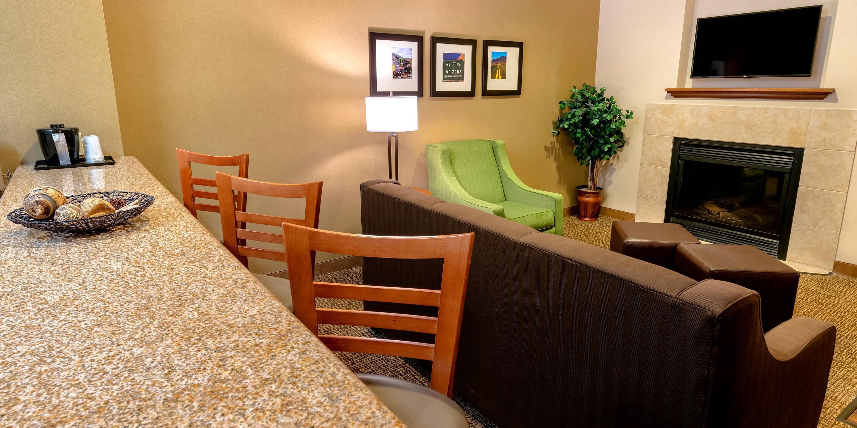 A hotel room with a dining area, a green armchair, a fireplace, and framed welcome signs.