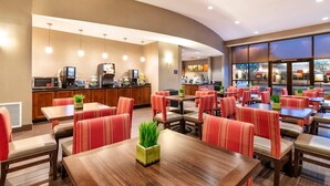 Un espace repas moderne avec des chaises à revêtement rouge, des tables en bois et une cuisine en arrière-plan.