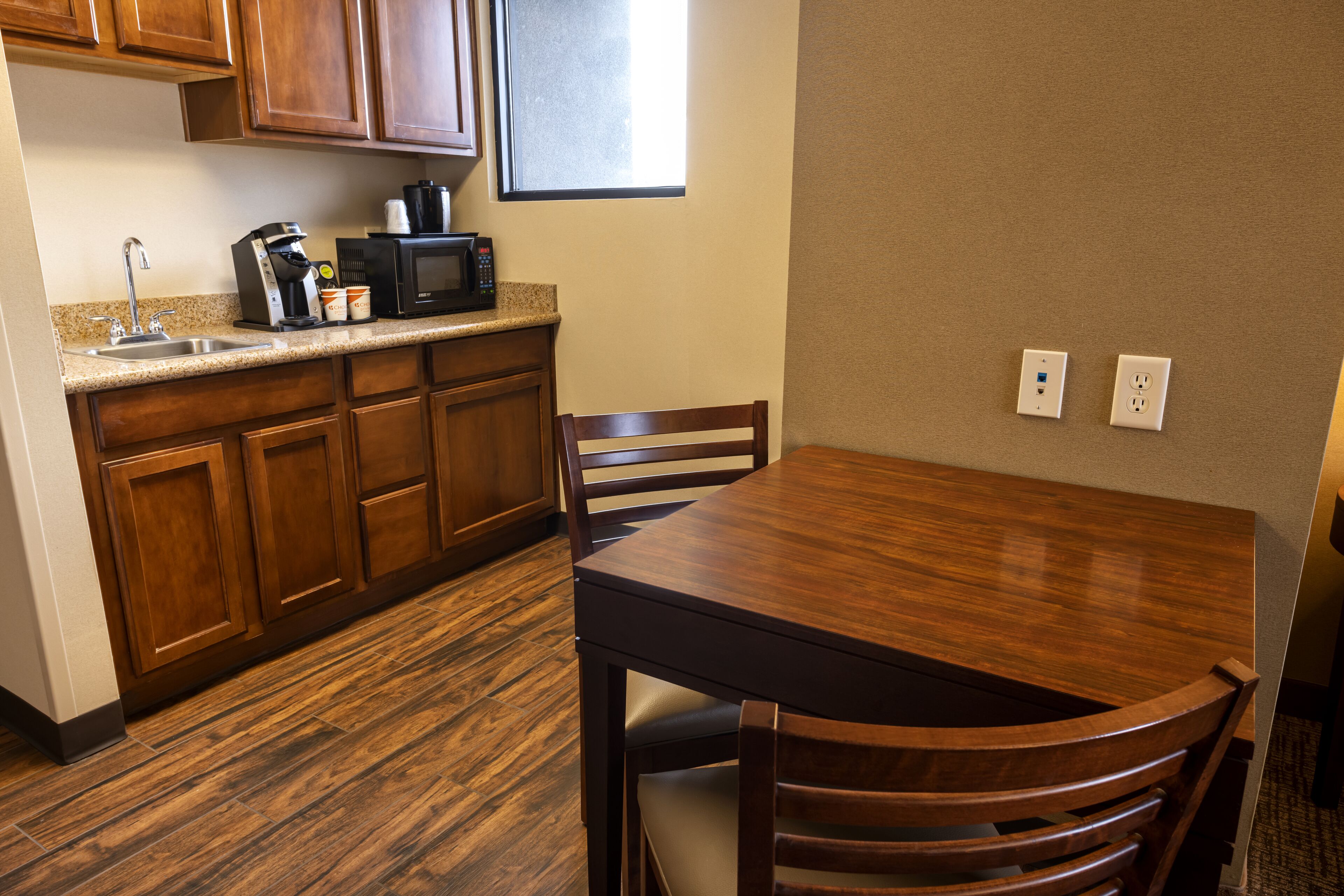 A compact kitchen with wooden cabinets, a granite countertop, a coffee maker, a microwave, and a dining table with chairs.