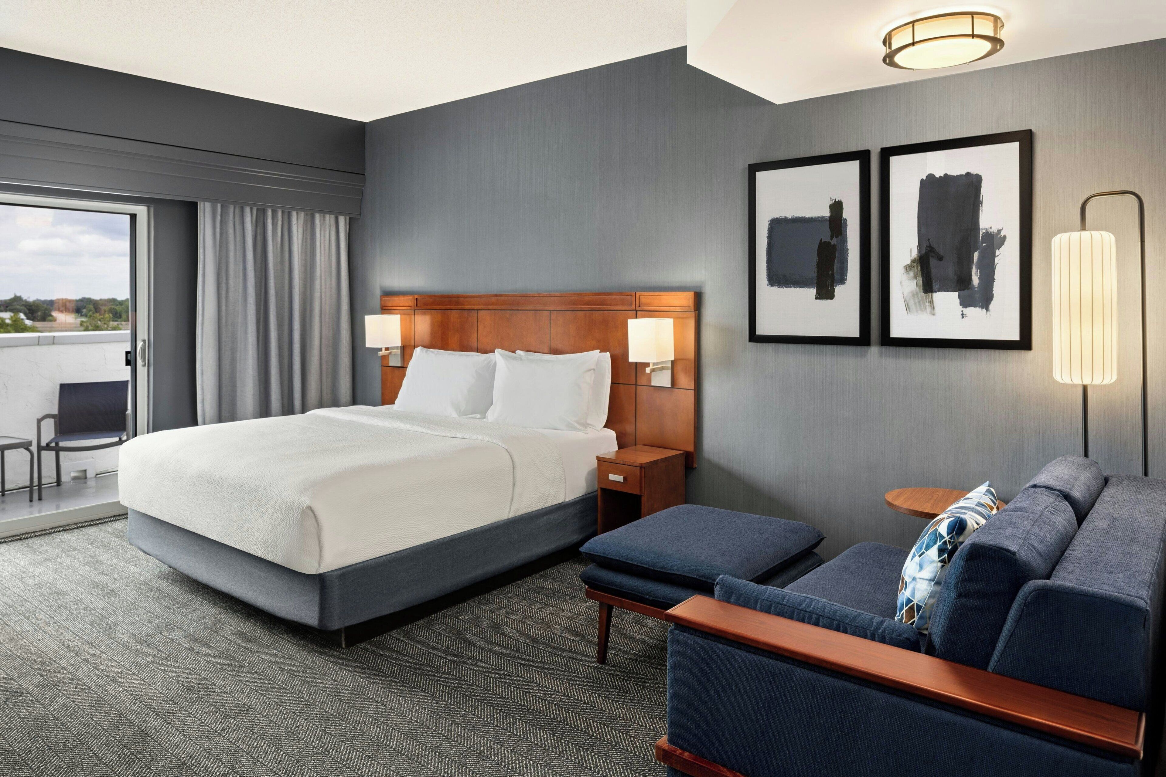 A hotel room with a large bed, a sofa, a small table, and two wall-mounted lamps.
