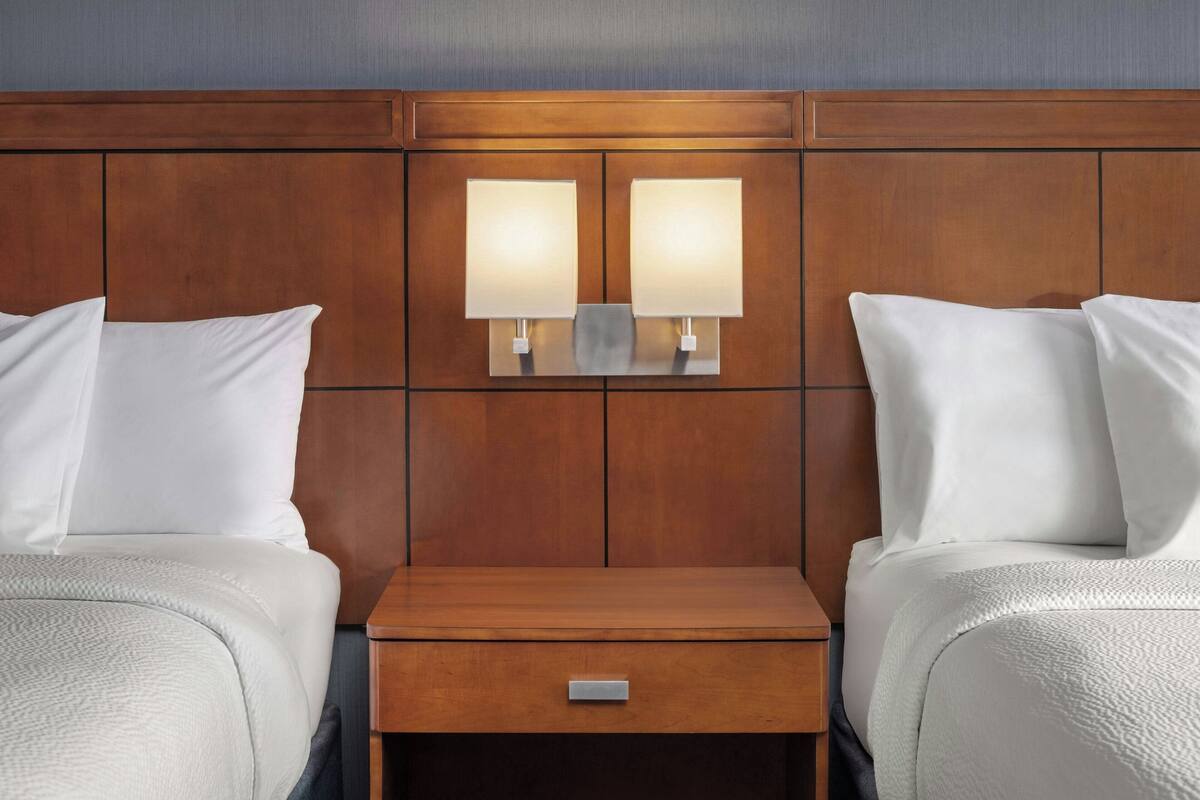 Een hotelkamer met twee bedden, een houten hoofdbord en een nachtkastje met een lade.