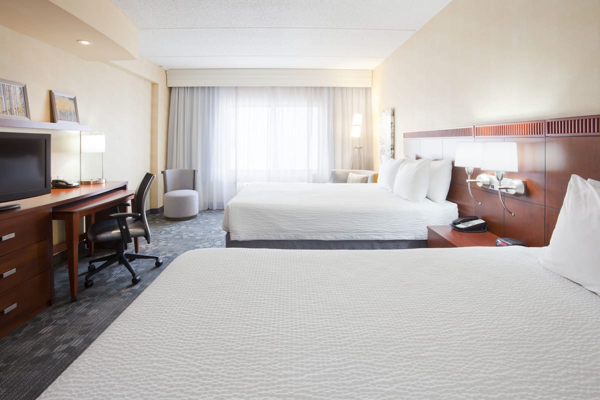 Een hotelkamer met twee bedden, een bureau met een stoel, een televisie en een lamp.