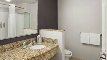 A bathroom with a granite countertop, a sink, a mirror, a toilet, and a towel rack.