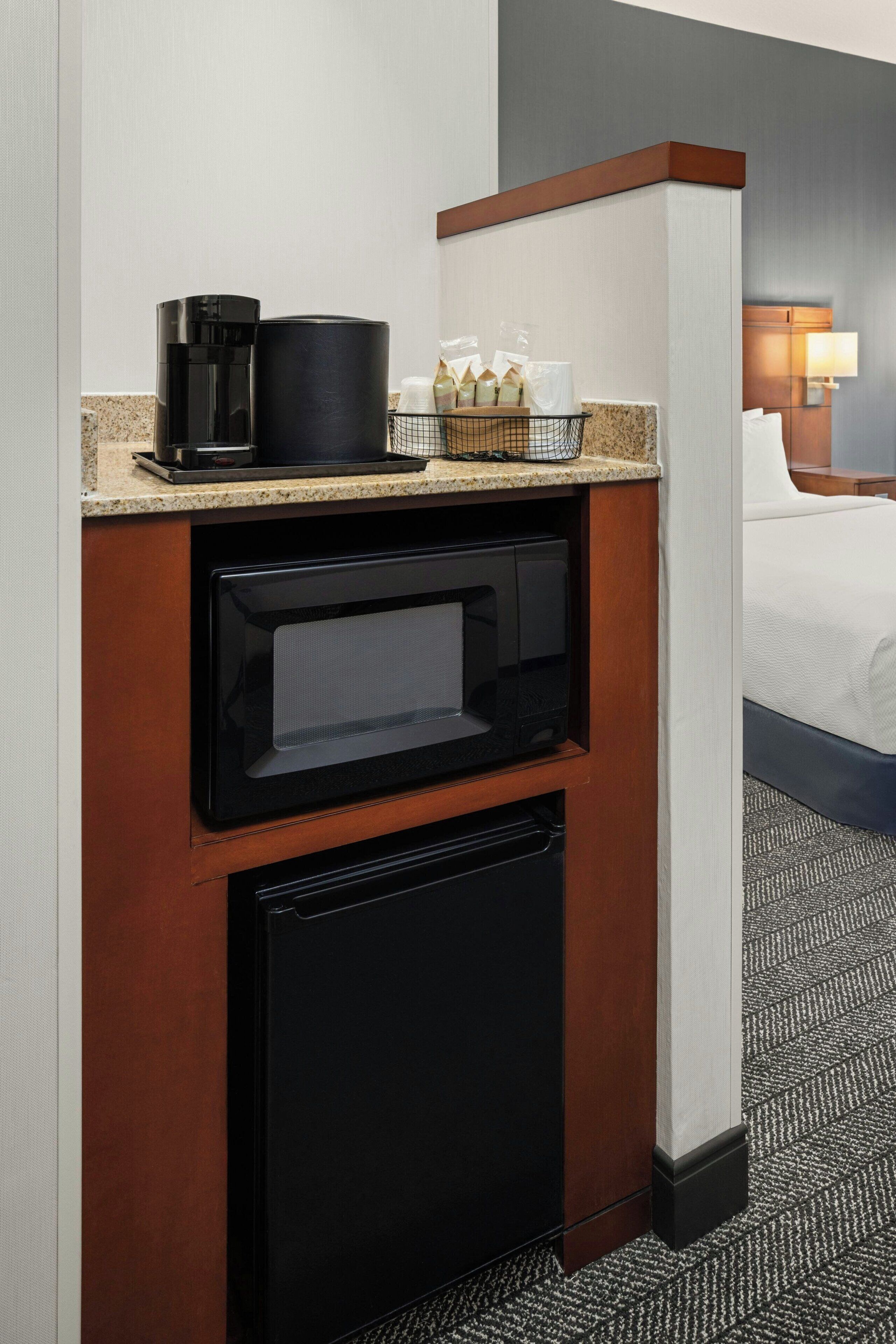 Una kitchenette compacta con cafetera, microondas y refrigerador pequeño.