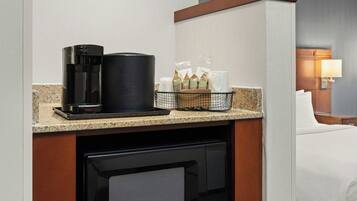 Una kitchenette compacta con cafetera, microondas y refrigerador pequeño.