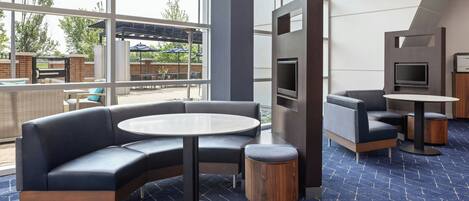 A modern lounge area with a curved sofa, round tables, and a TV screen.