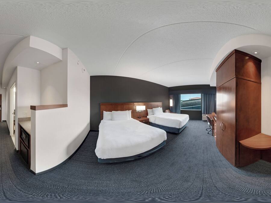 A modern hotel room with a curved ceiling, two beds, a desk, and a wardrobe.