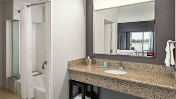 A modern bathroom with a granite countertop sink, a large mirror, and a shower area.