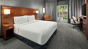 Habitación de hotel con una cama grande, dos lámparas de noche, una silla, un escritorio con un televisor y vistas al exterior a través de una puerta corrediza.