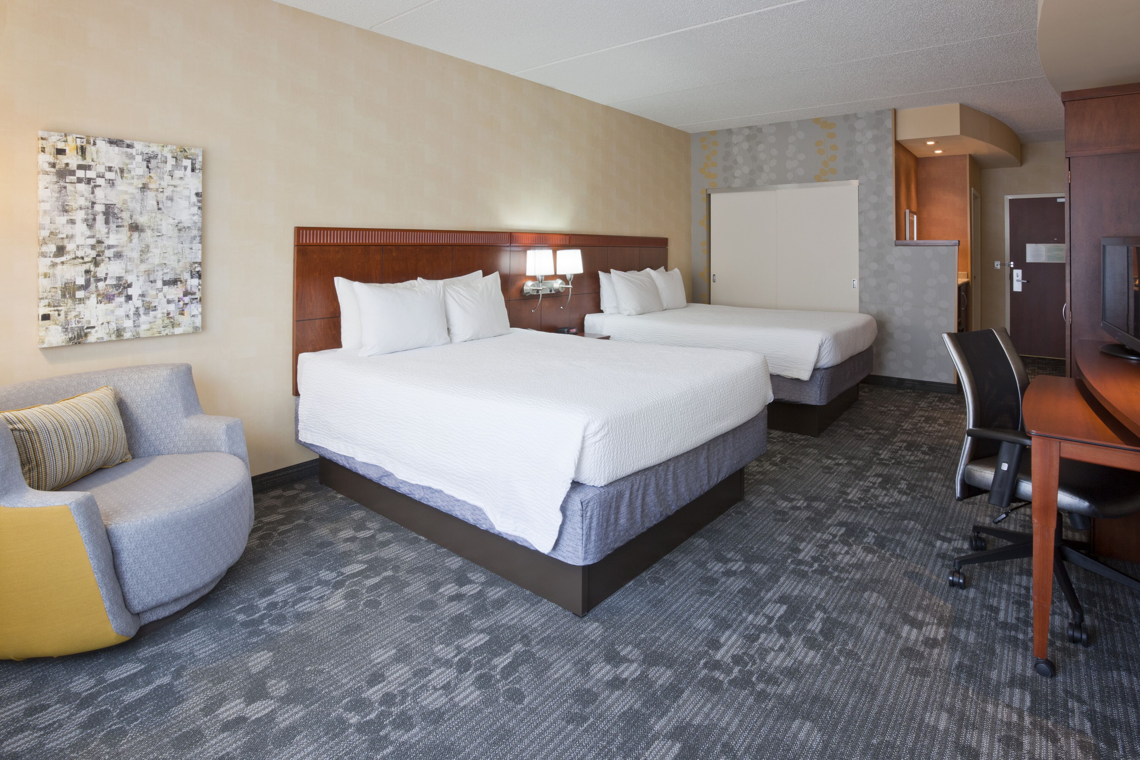 Une chambre d’hôtel avec deux lits, un bureau, une chaise et un grand tableau abstrait accroché au mur.